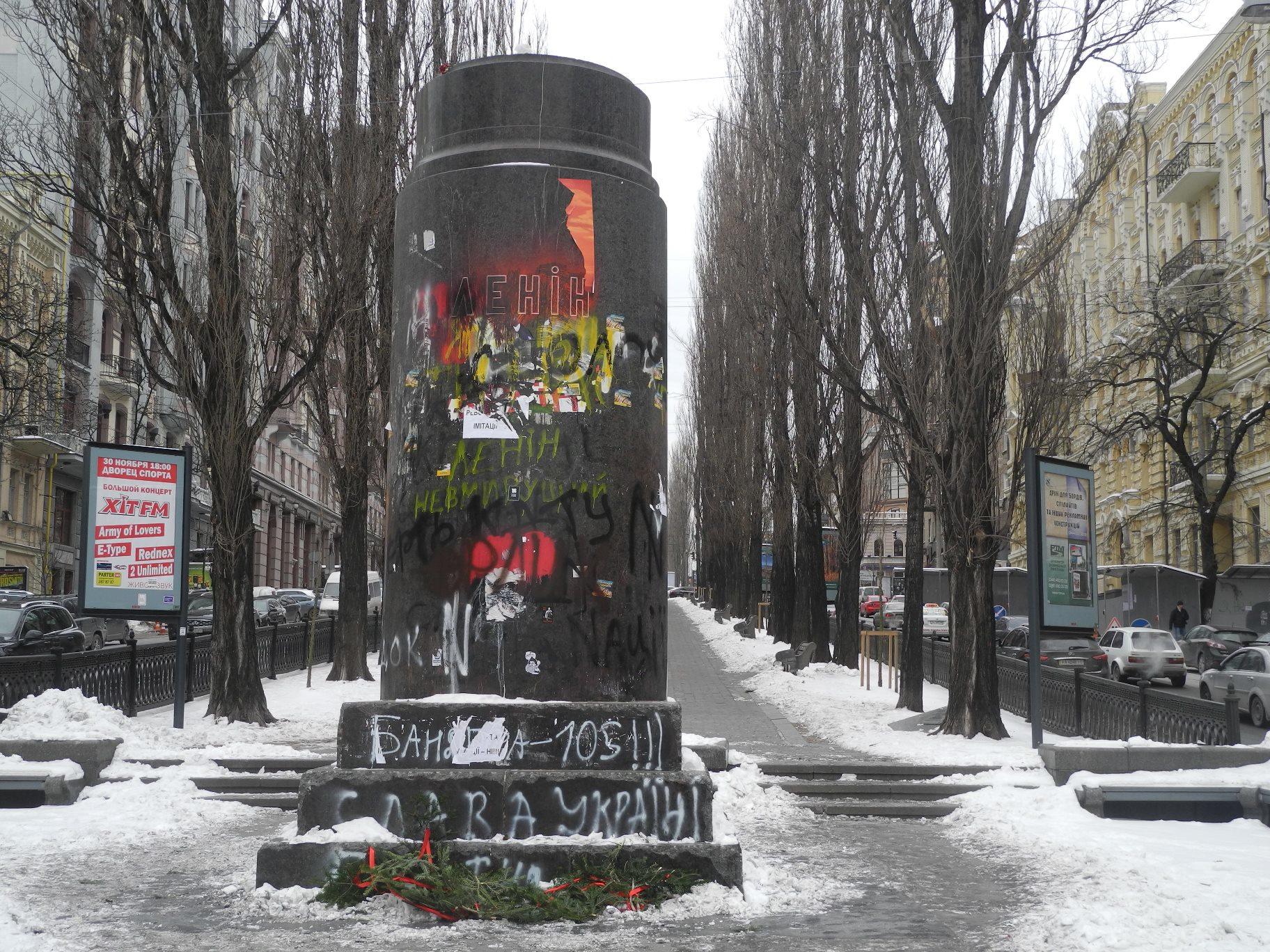 In der Bildmitte steht ein großer Sockel aus dunkelgrauem Granit mit der kyrillischen Aufschrift "Lenin". Der Sockel ist mit Graffiti besprüht. Die Statue fehlt.